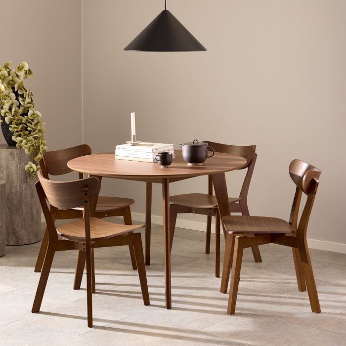 Wooden dining set with round table and chairs in a room with a beige wall and black pendant light.