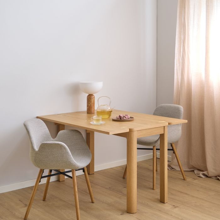 Dining area with wooden table and chairs in a room with light-colored walls and curtains.