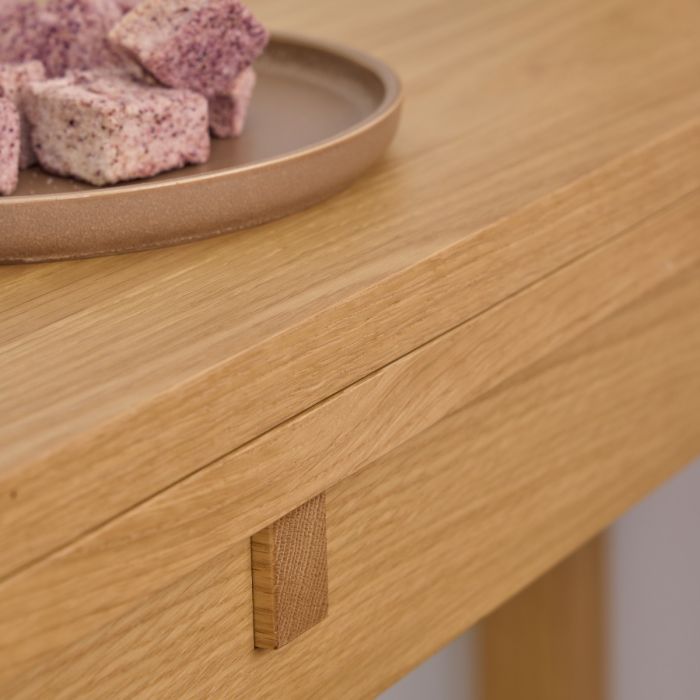 Wooden table with a close-up of a drawer handle and a plate of pink and purple food in the background.