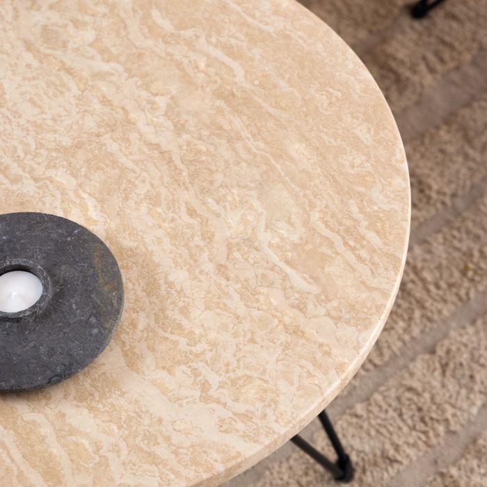 Round beige marble table with a black metal base on a textured surface