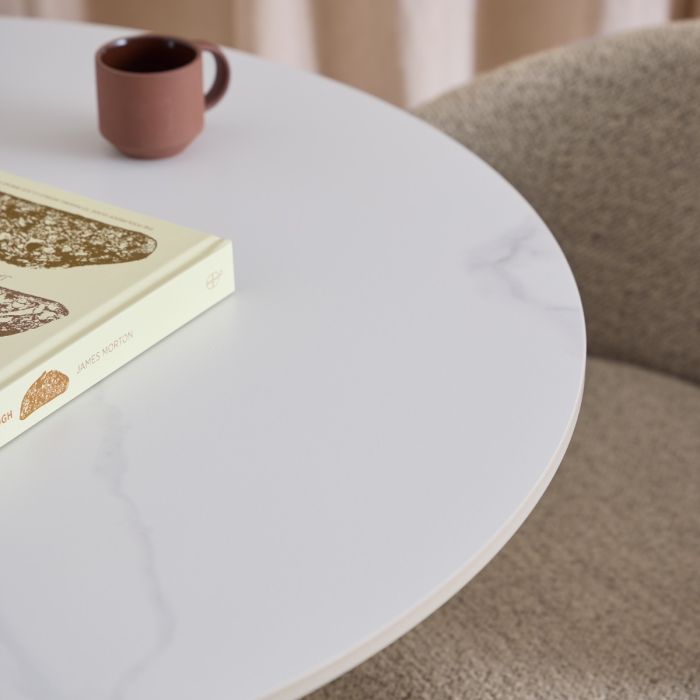 Round white table with a book and a brown mug on top, blurred background