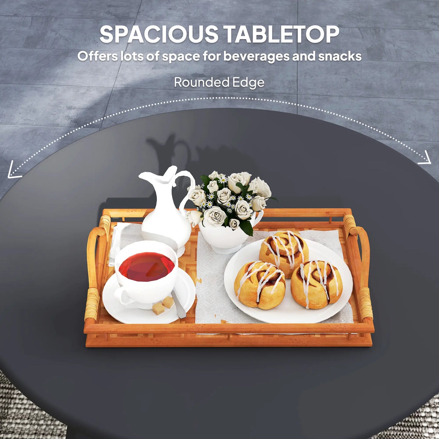 Round black table with a wooden tray holding tea set, flowers, and pastries on a dark surface.