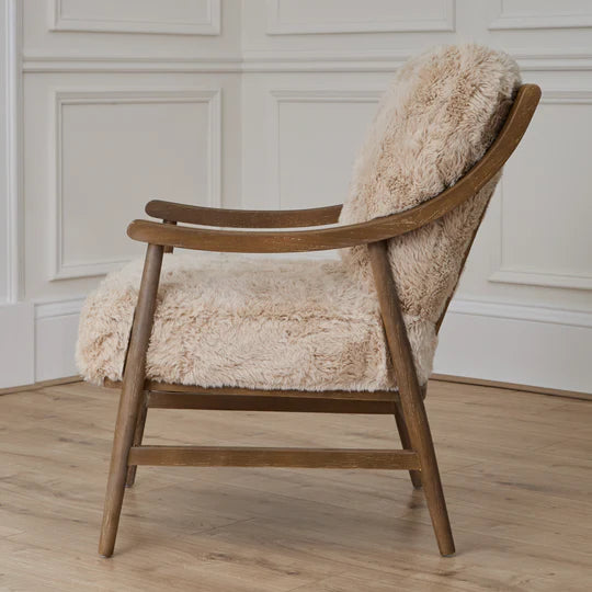 Wooden armchair with beige fur upholstery in a room with wooden flooring and white paneled walls.