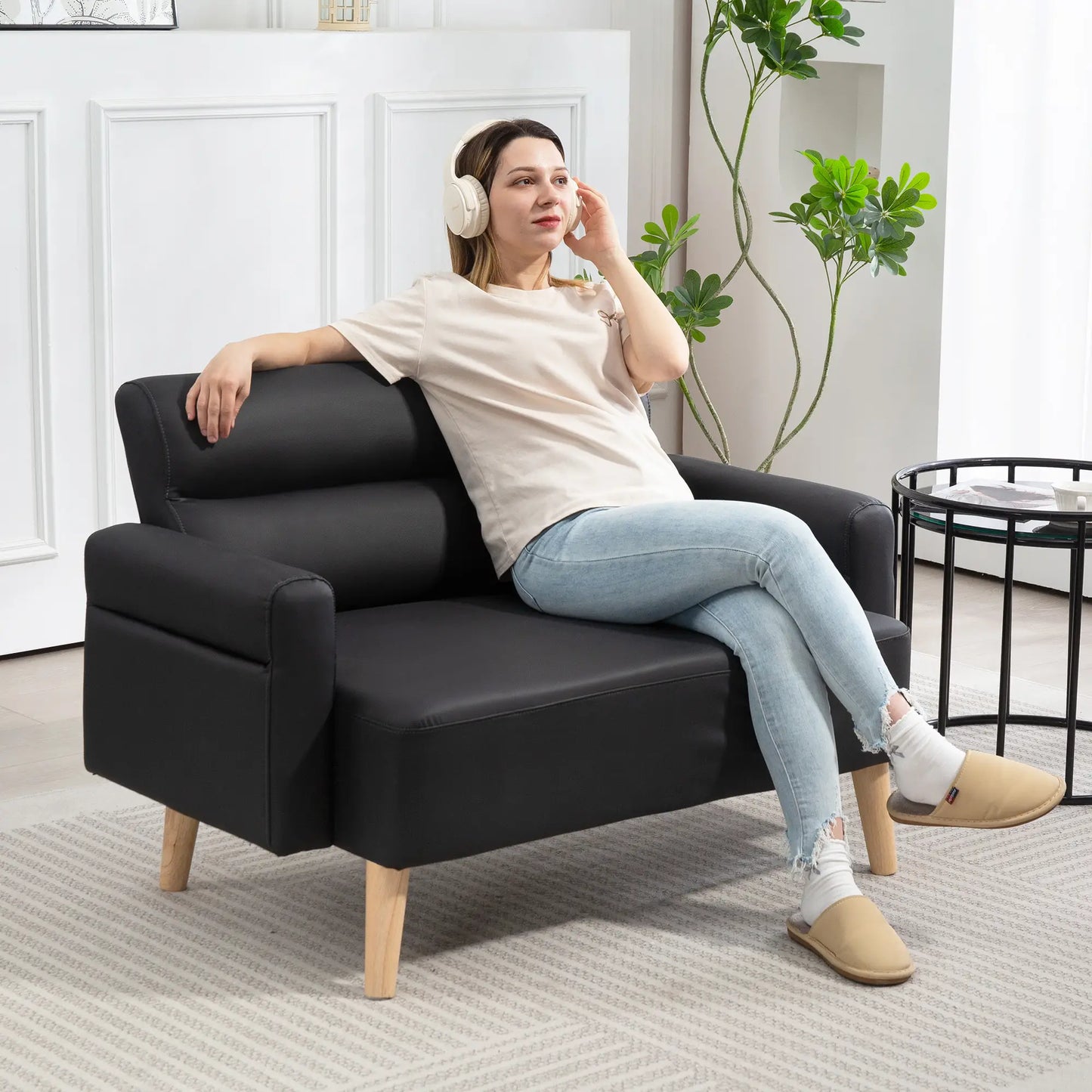 Woman sitting on a black sofa wearing headphones in a modern living room.