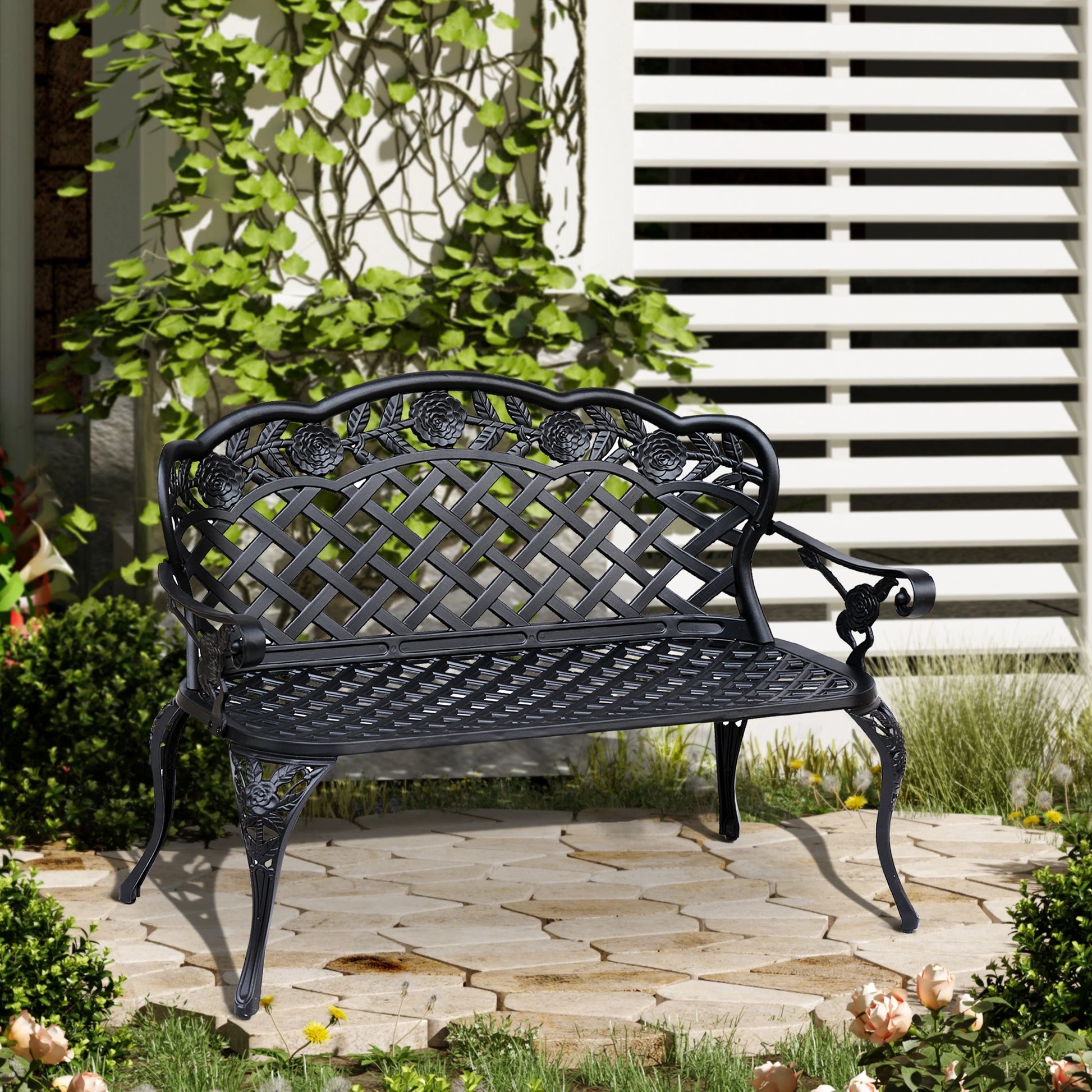 Black metal garden bench in a garden setting with plants and a white lattice background.
