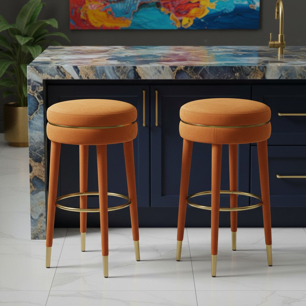 Two orange bar stools with gold accents in front of a kitchen island with a colorful abstract painting above.