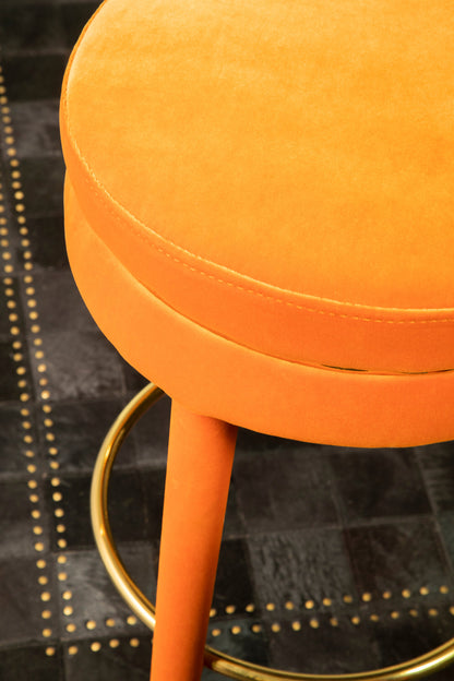 Close-up of an orange stool with gold legs on a black textured surface.