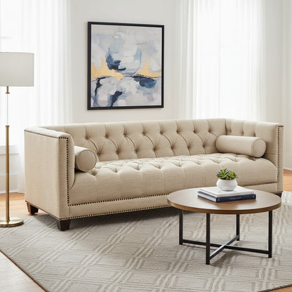Beige tufted sofa in a living room with a round wooden coffee table and abstract art on the wall.