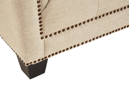 Close-up of a beige upholstered chair with nailhead trim on a white background
