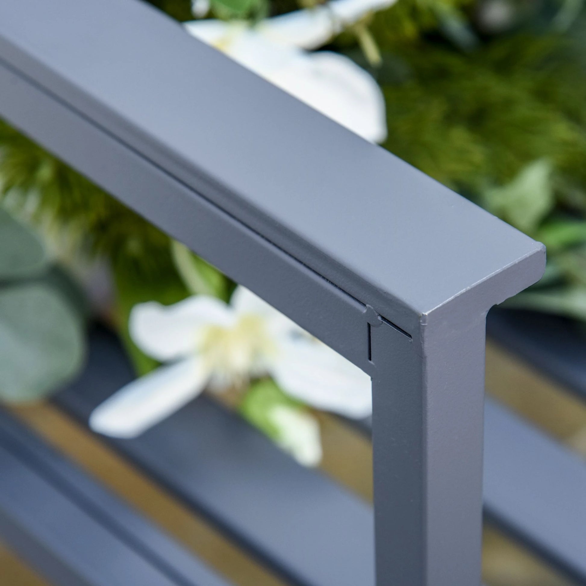 Close-up of a gray metal frame with blurred greenery and white flowers in the background