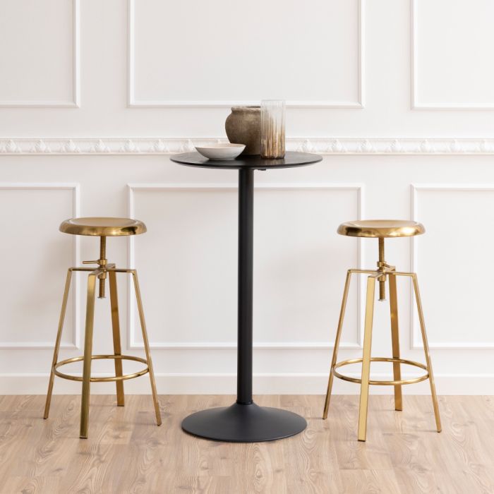 Black bar table with two gold bar stools against a white paneled wall.