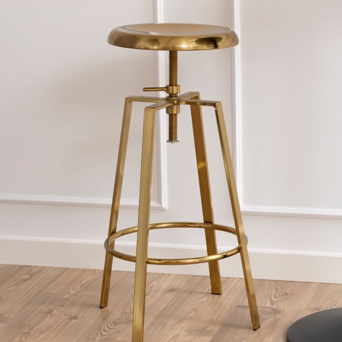 Gold metal bar stool on a wooden floor with a white wall background