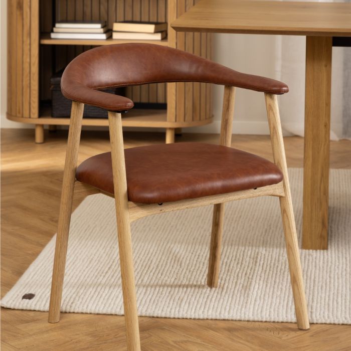 Brown leather chair with wooden frame on a rug in a room with a table and shelves.