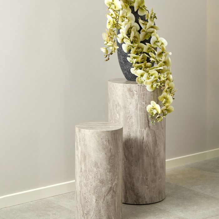 Two cylindrical stone pedestals with a vase of green flowers against a plain wall.