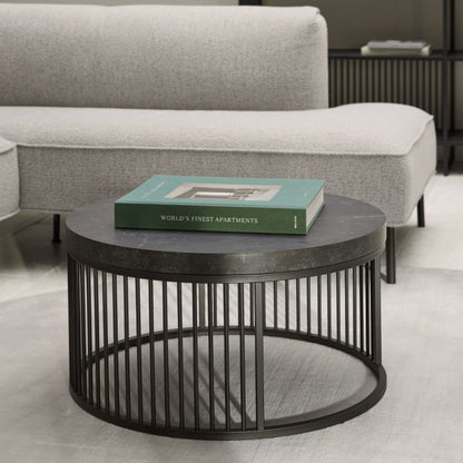 Round black metal coffee table with a book on top in a living room setting.