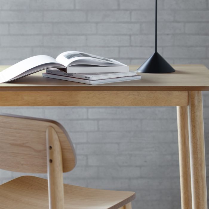 Wooden desk with an open book and a black pendant light, against a gray brick wall.