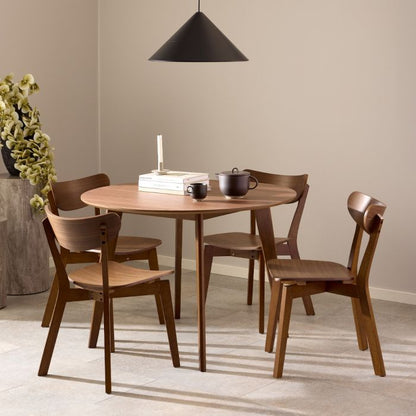 Wooden dining set with round table and chairs in a room with a beige wall and black pendant light.