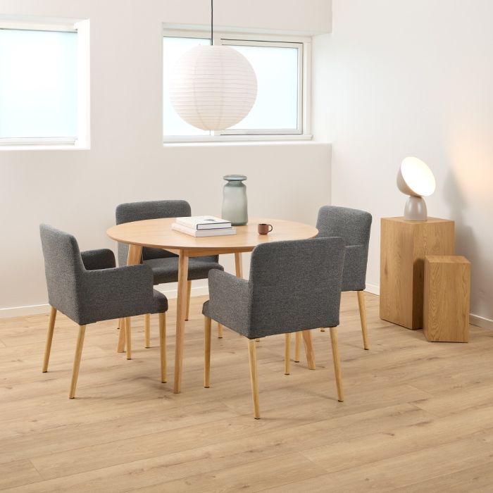 Dining area with round wooden table and gray chairs in a room with light wood flooring and white walls.