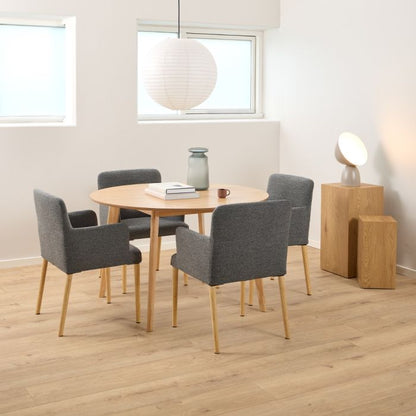 Dining area with round wooden table and gray chairs in a room with light wood flooring and white walls.