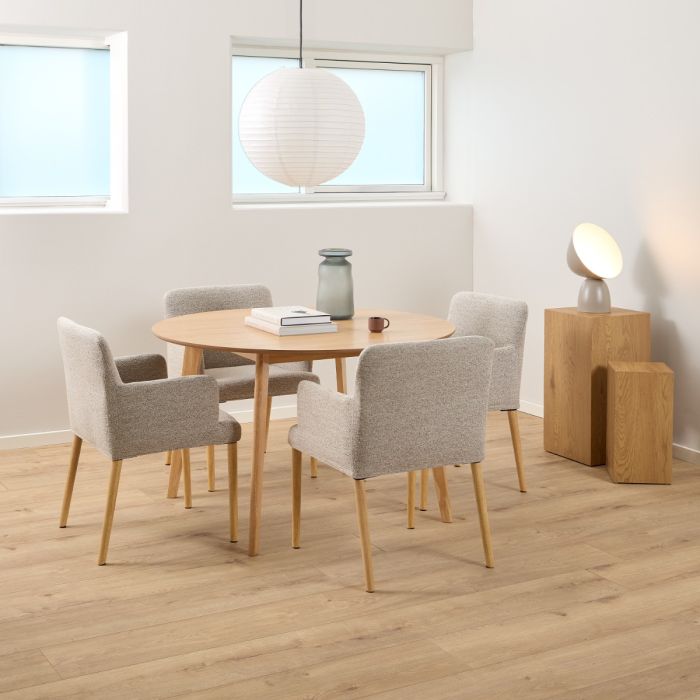 Dining area with round wooden table and four gray chairs in a bright room.