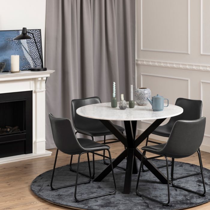 Dining room with a round marble table and black chairs in front of a fireplace.