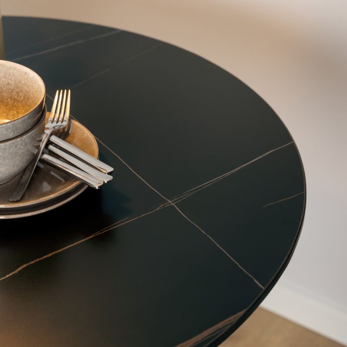 Black round table with a stack of plates, cups, and cutlery on a neutral background