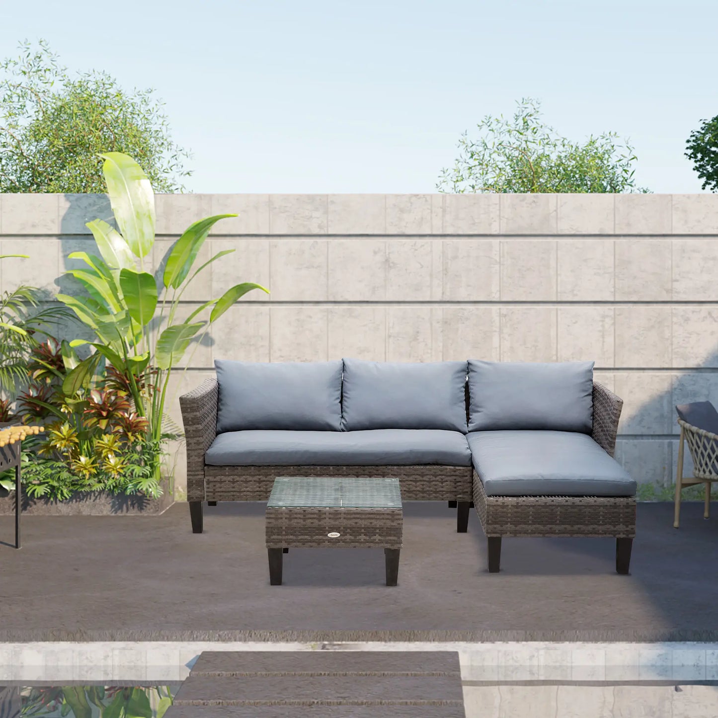 Outdoor patio furniture set with gray cushions on a patio with plants and a wall in the background.