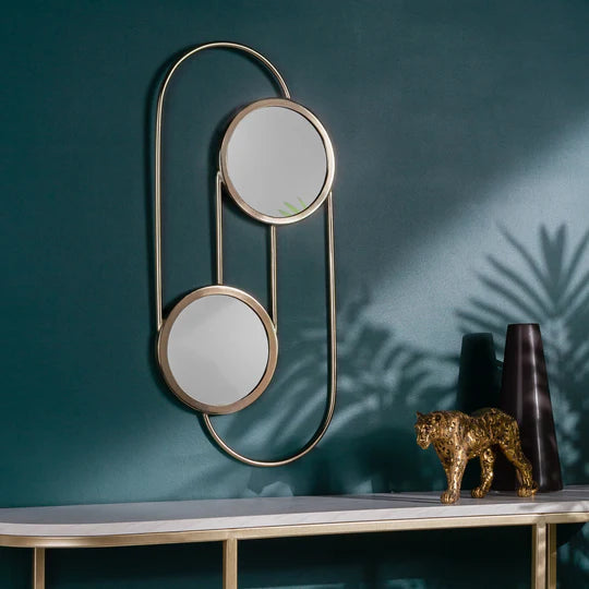 Decorative wall mirror with two round mirrors on a teal wall with a table and decorative items.