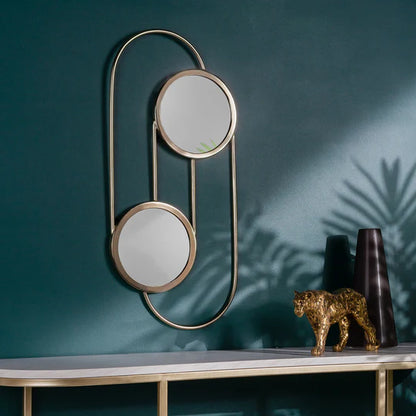 Decorative wall mirror with two round mirrors on a teal wall with a table and decorative items.