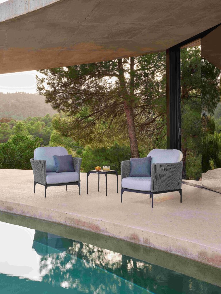 Outdoor patio set with chairs and table by a poolside, surrounded by greenery.