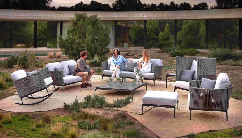 People sitting on outdoor furniture in a modern patio setting with greenery.