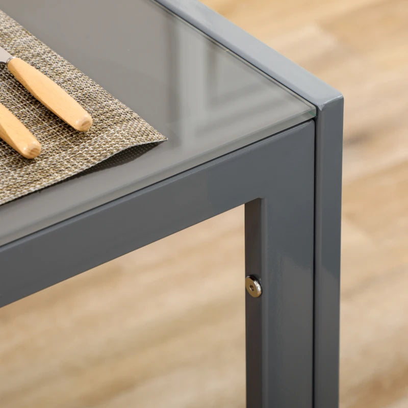 Gray metal table corner with a glass top and wooden items on a wooden floor.