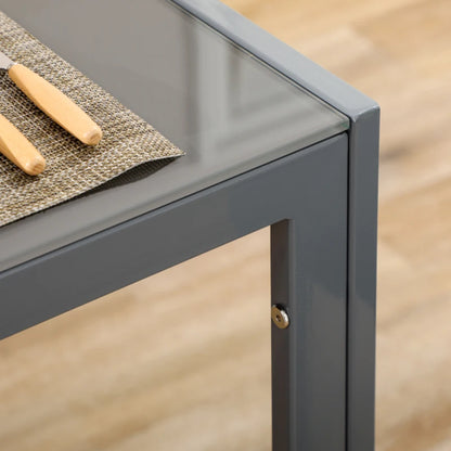 Gray metal table corner with a glass top and wooden items on a wooden floor.