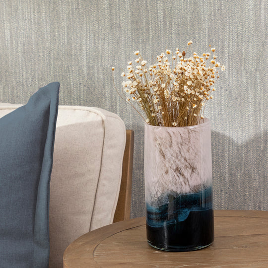 Decorative vase with dried flowers on a wooden table against a textured wall.