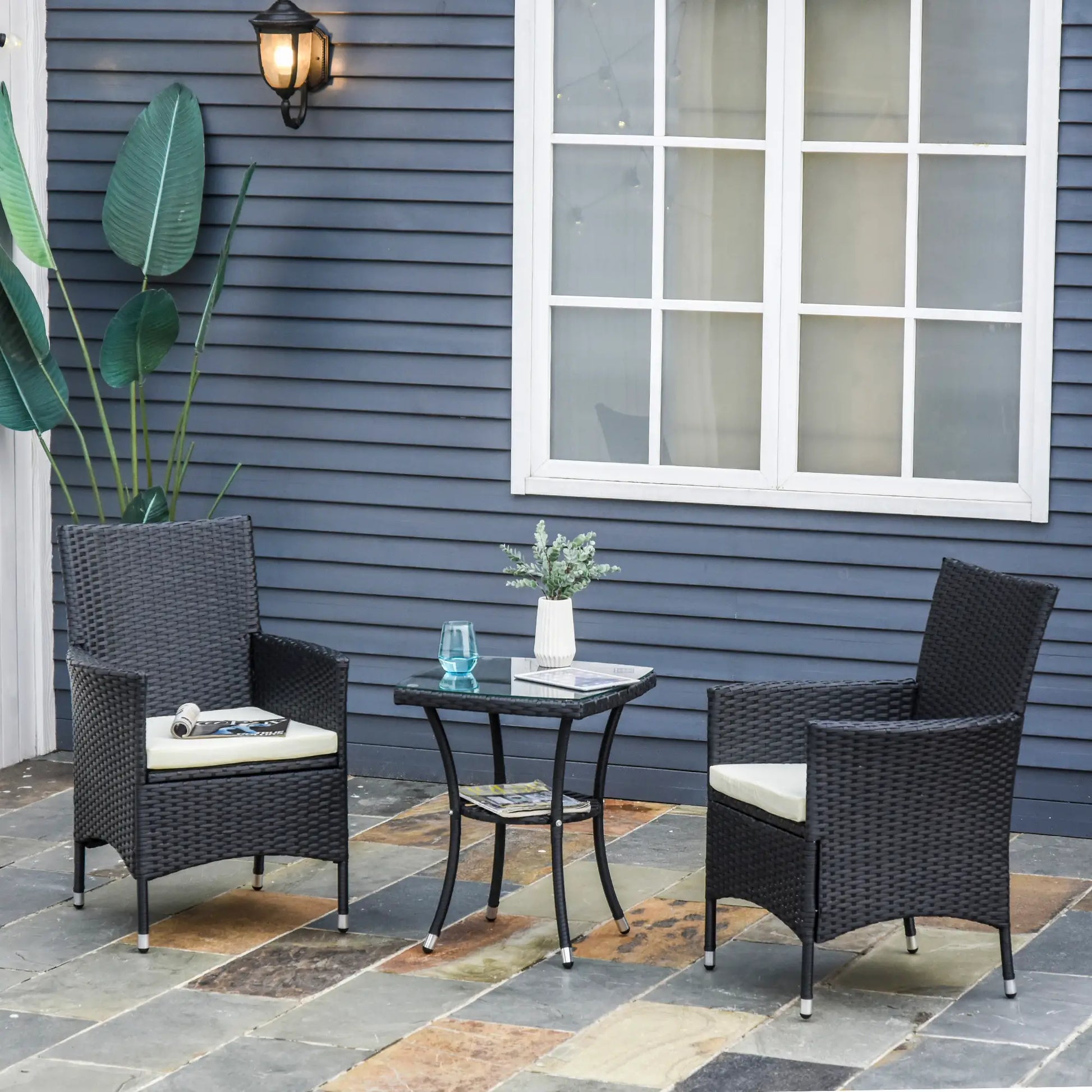 Outdoor patio set with two chairs and a small table on a stone patio against a blue house.