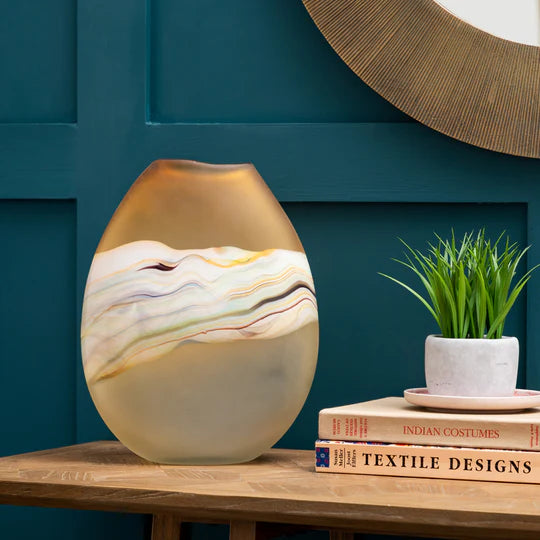 Decorative vase on a wooden surface with a teal wall and books in the background
