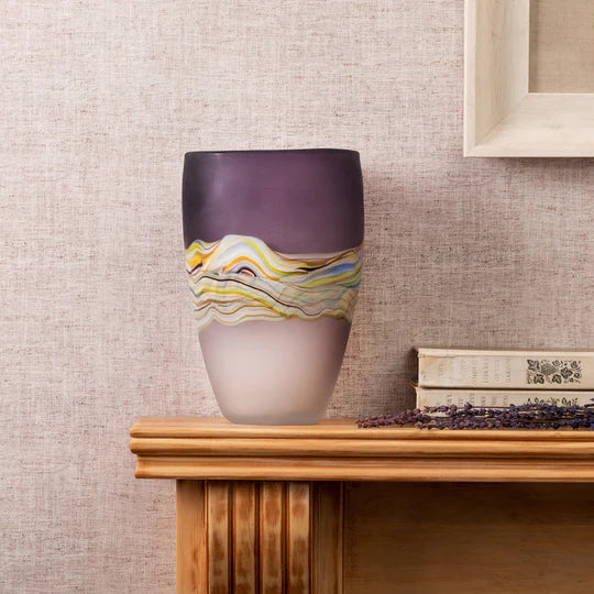 Decorative vase with wavy pattern on a wooden surface against a textured wall.