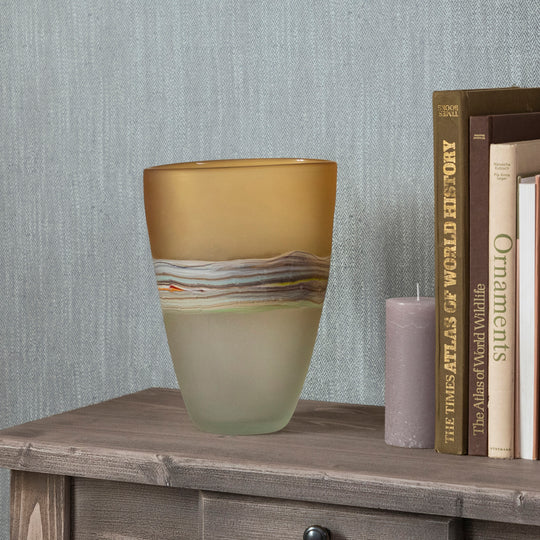 Decorative glass vase on a wooden surface with books and a candle in the background.