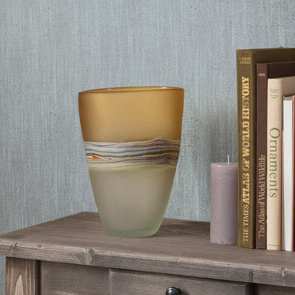 Decorative glass vase on a wooden surface with books and a candle in the background.