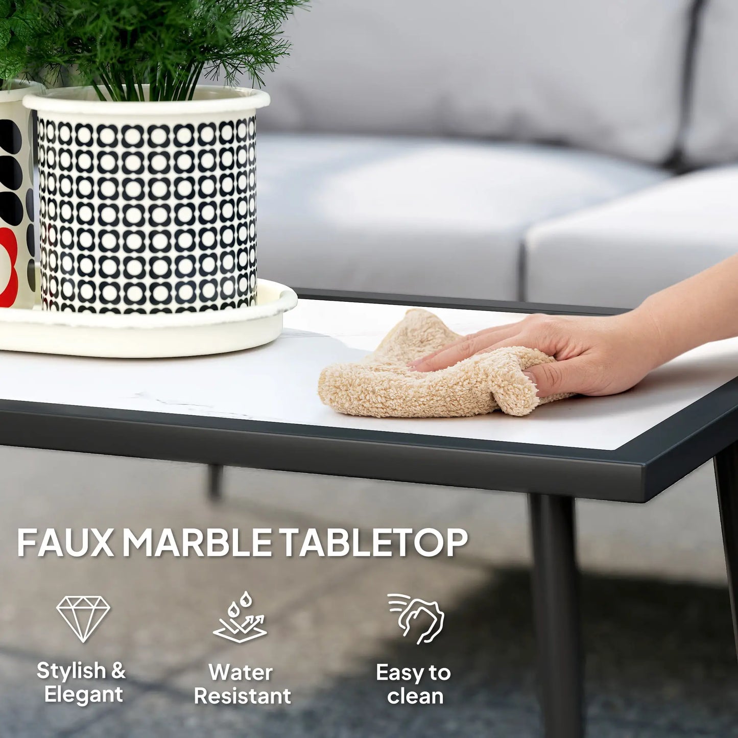 Faux marble tabletop with a hand wiping a surface, potted plant, and gray sofa in the background.