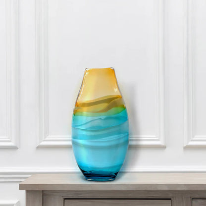 Glass vase with blue and yellow gradient on a wooden surface against a white paneled wall
