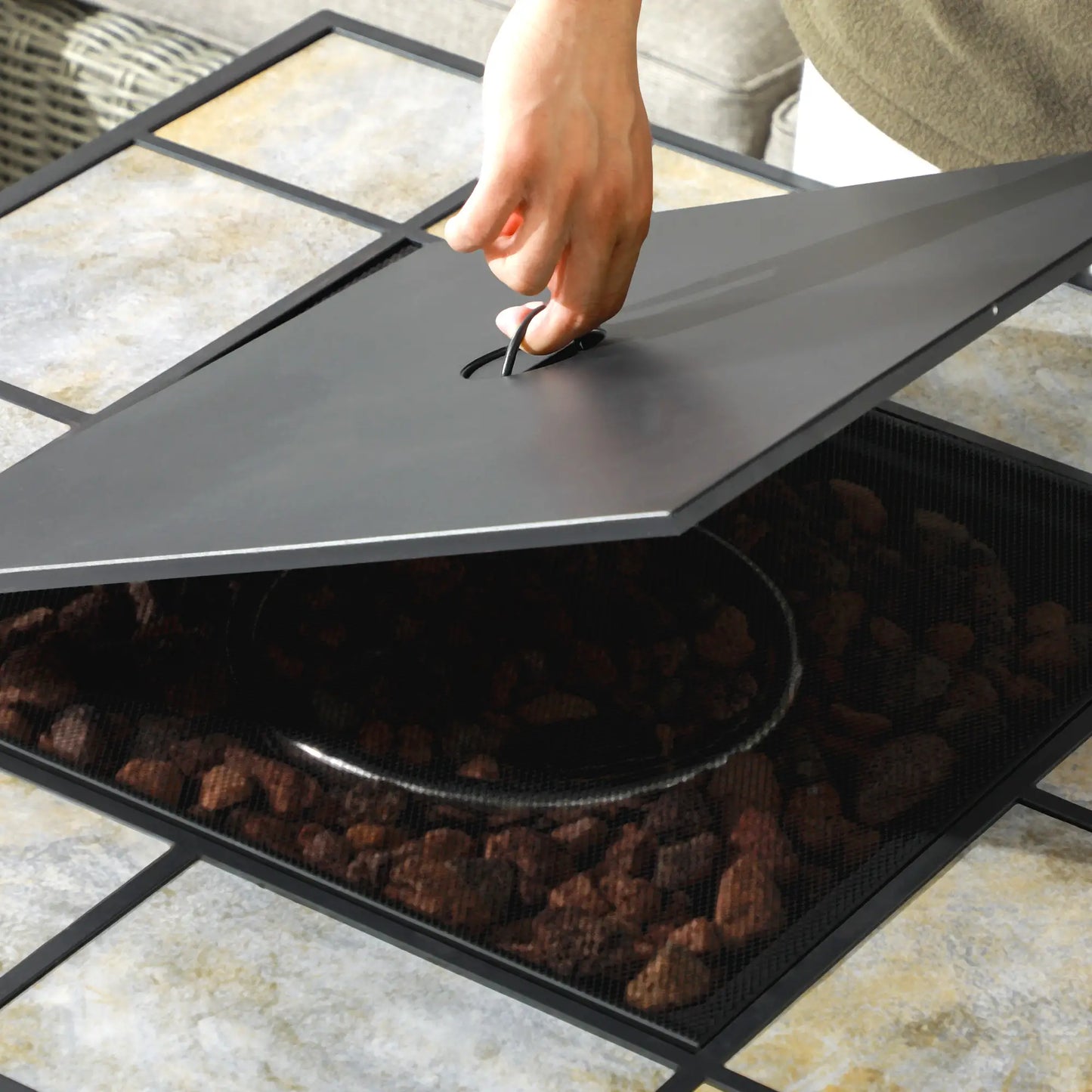 Person opening a black fire pit lid on a tiled floor