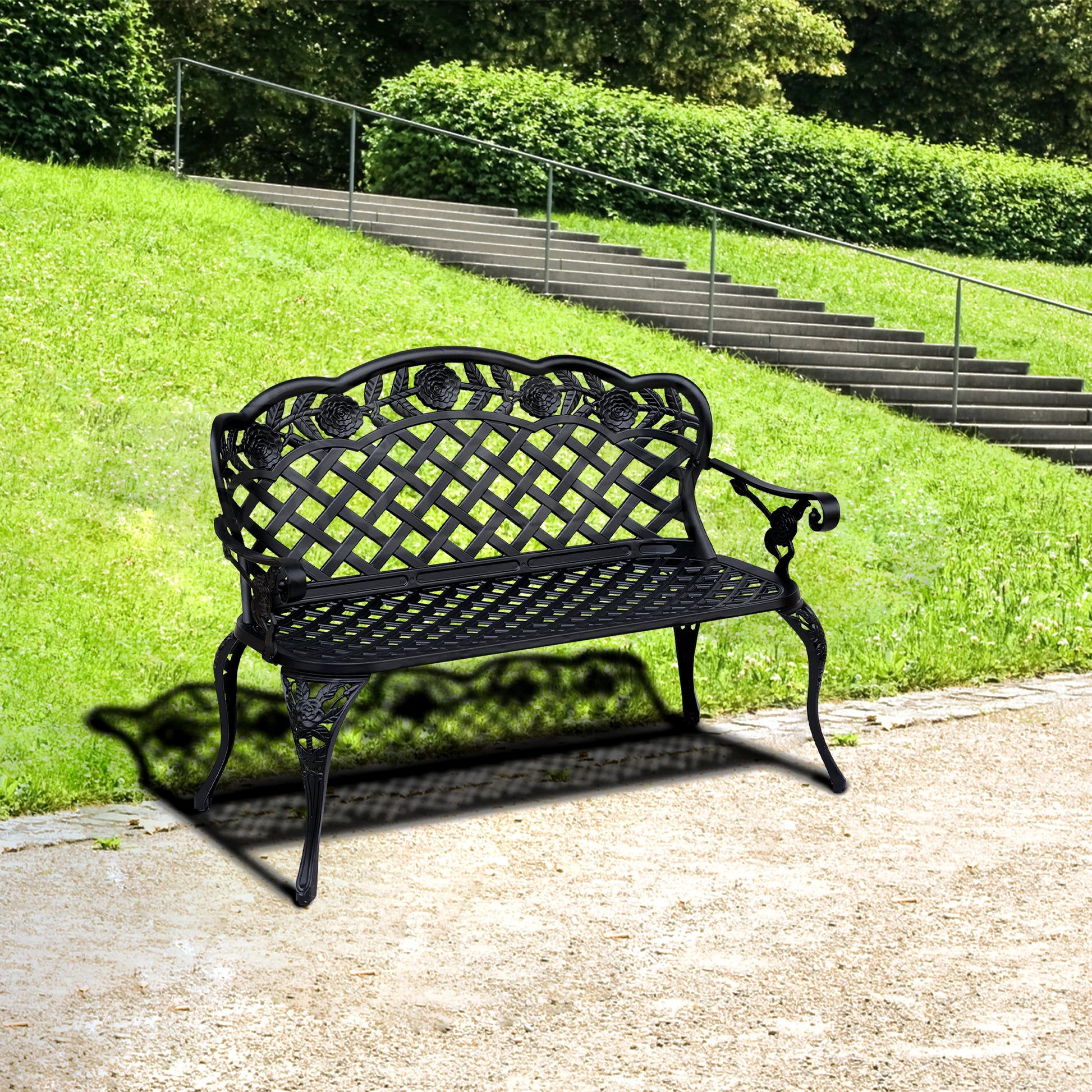 Black metal garden bench on a concrete path with green grass and stairs in the background