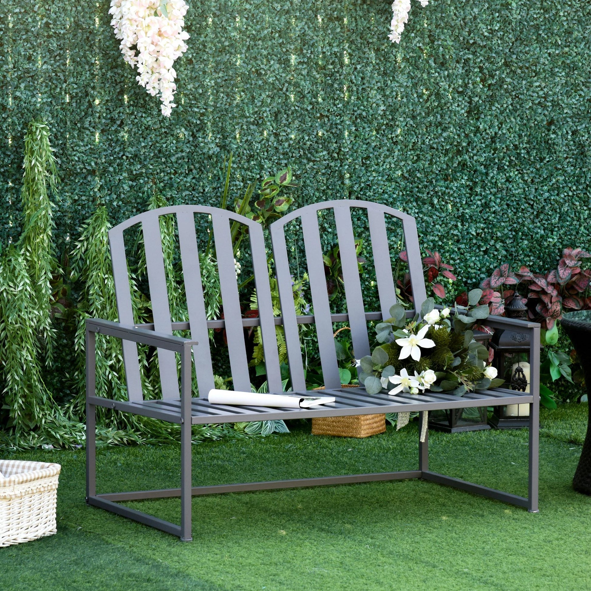 Gray metal bench in a garden setting with greenery and flowers.