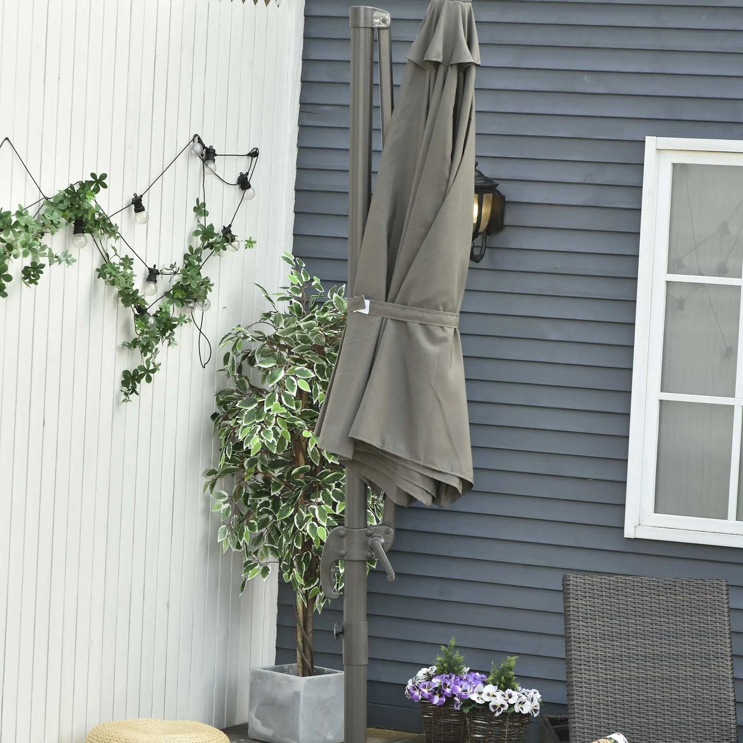 Gray outdoor umbrella on a stand against a gray house exterior with plants and a chair.