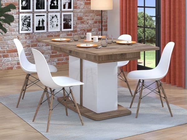 Dining table with white chairs in a room with a brick wall and large window.