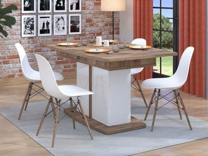 Dining table with white chairs in a room with a brick wall and large window.