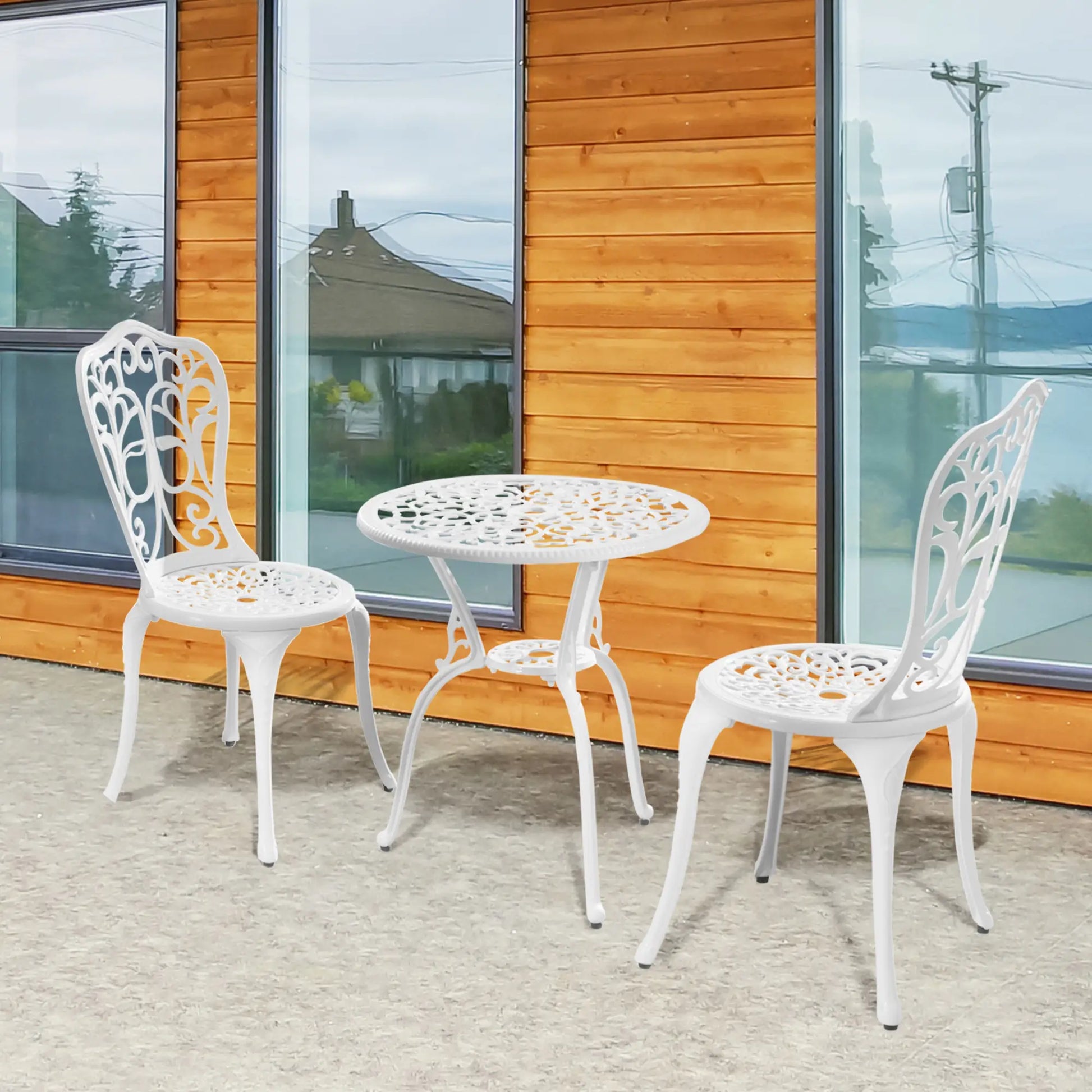 White metal outdoor table and chairs in front of a wooden building with glass windows.