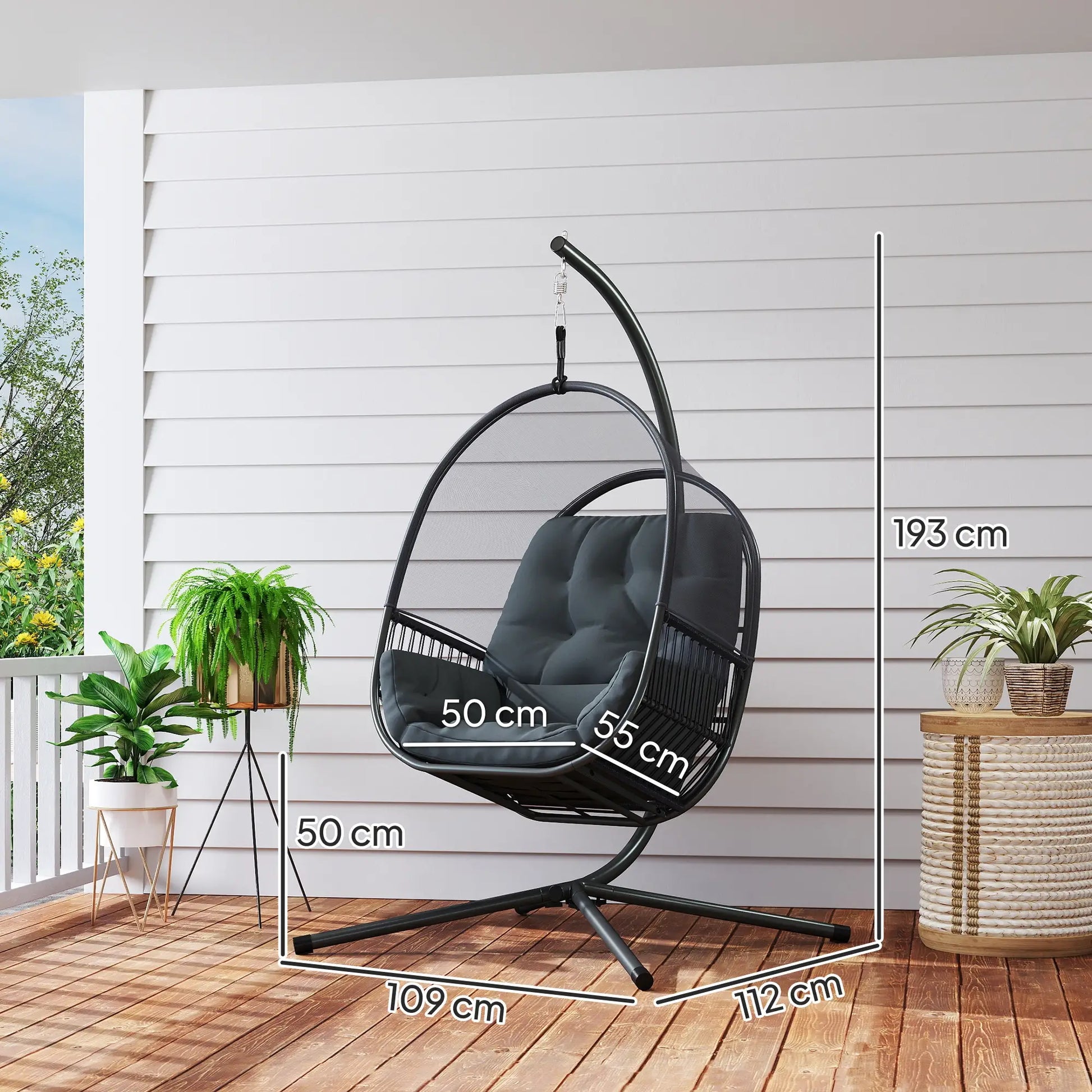 Black hanging egg chair with dimensions on a wooden deck with plants and a white wall.