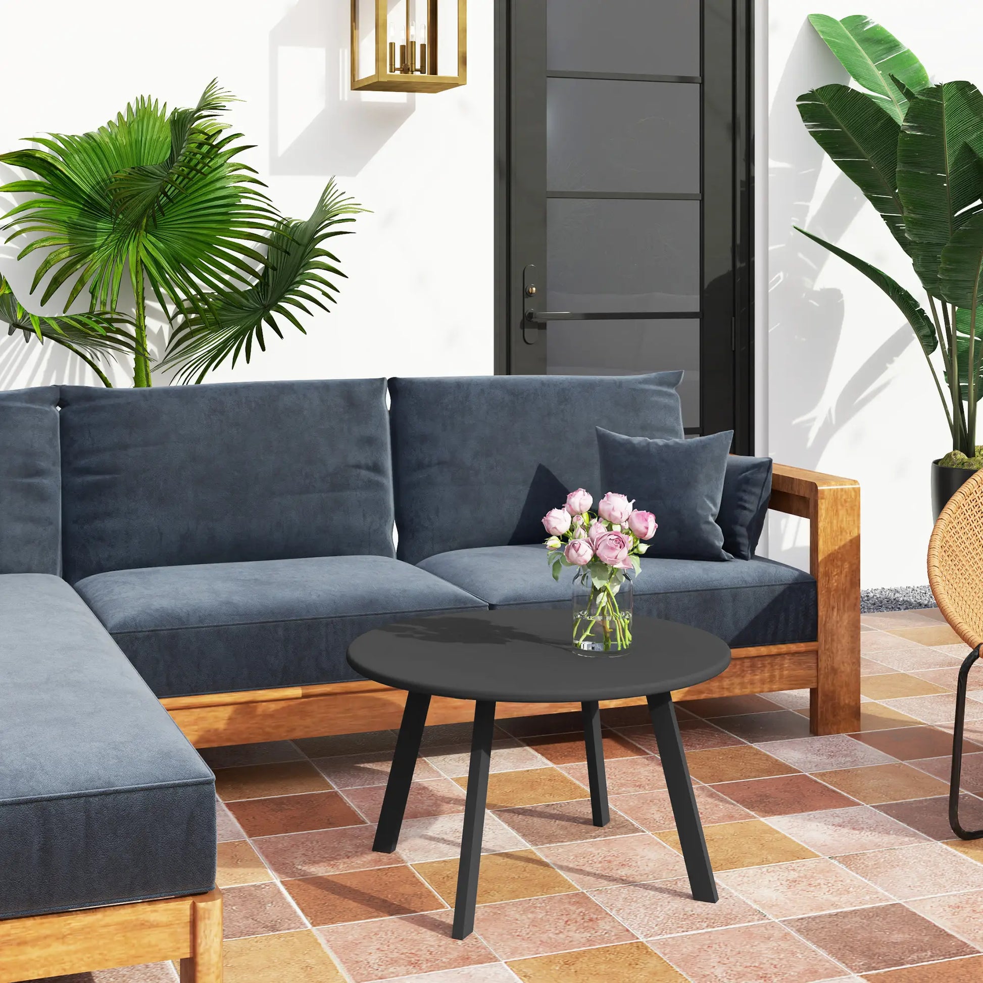 Blue sectional sofa with a small black table and pink flowers on a patio with plants and a door in the background.